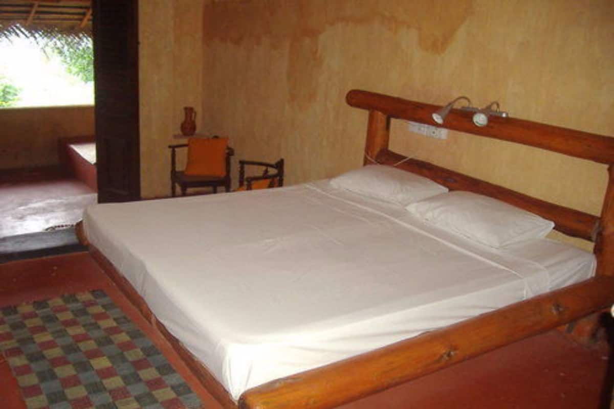 A single bed with a wooden headboard, a small table with a chair, and a checkered mat on the floor.
