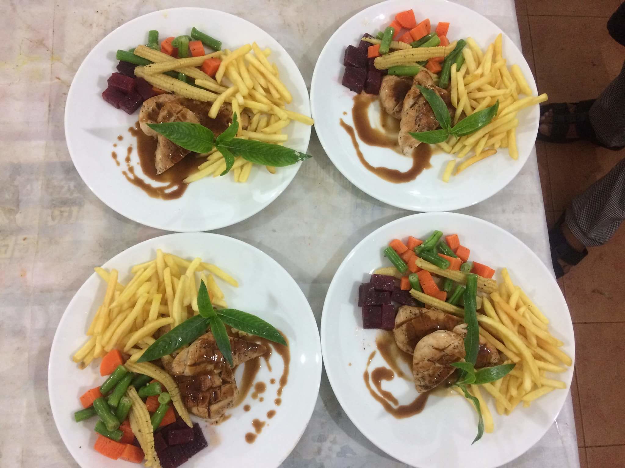 Vier borden eten met vlees, groenten en friet.