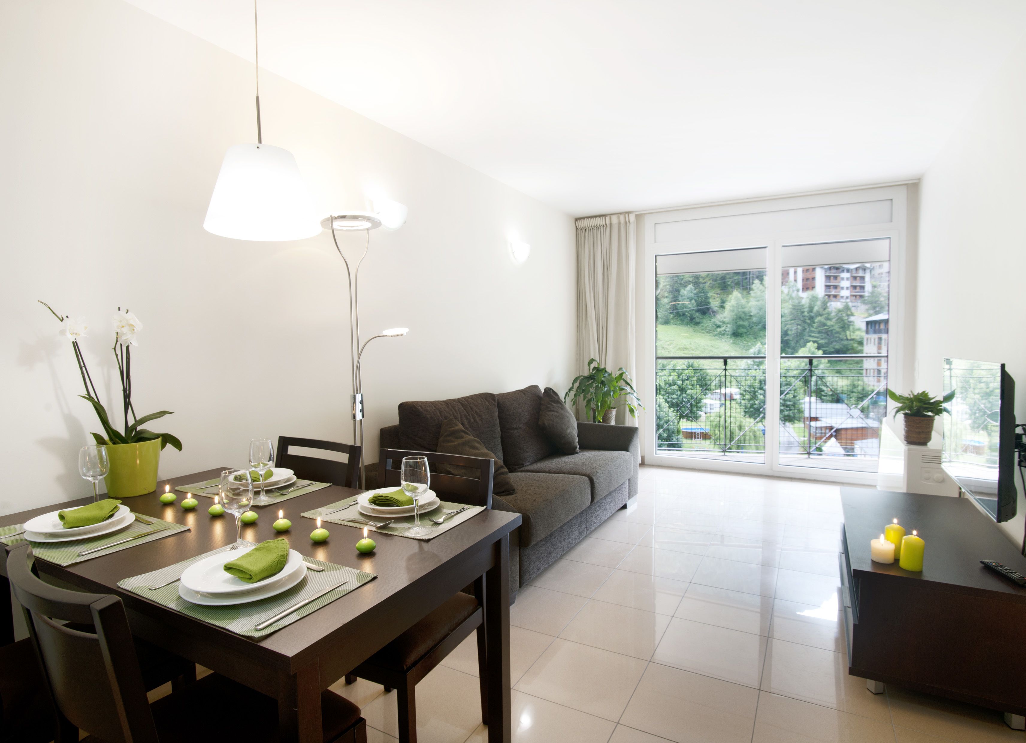 Un coin repas avec une table dressée pour deux personnes, un canapé et un balcon offrant une vue agréable.