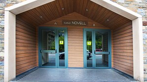 Une entrée moderne, avec des lambris en bois et des murs en pierre, agrémentée de deux portes en verre et d’une enseigne placée au-dessus.