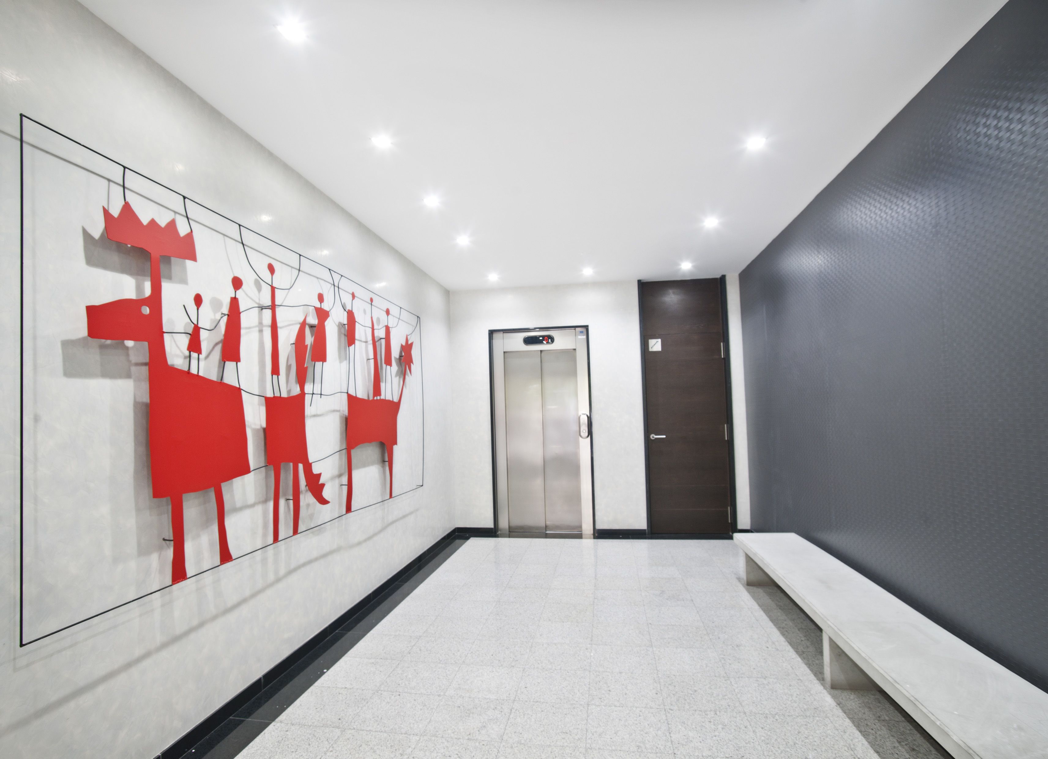 Un pasillo moderno con una gran obra de arte abstracta roja a la izquierda, un banco a la derecha y una puerta al final.