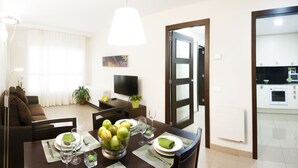 Un coin repas avec une table dressée pour deux personnes, un saladier de fruits et un téléviseur en arrière-plan.
