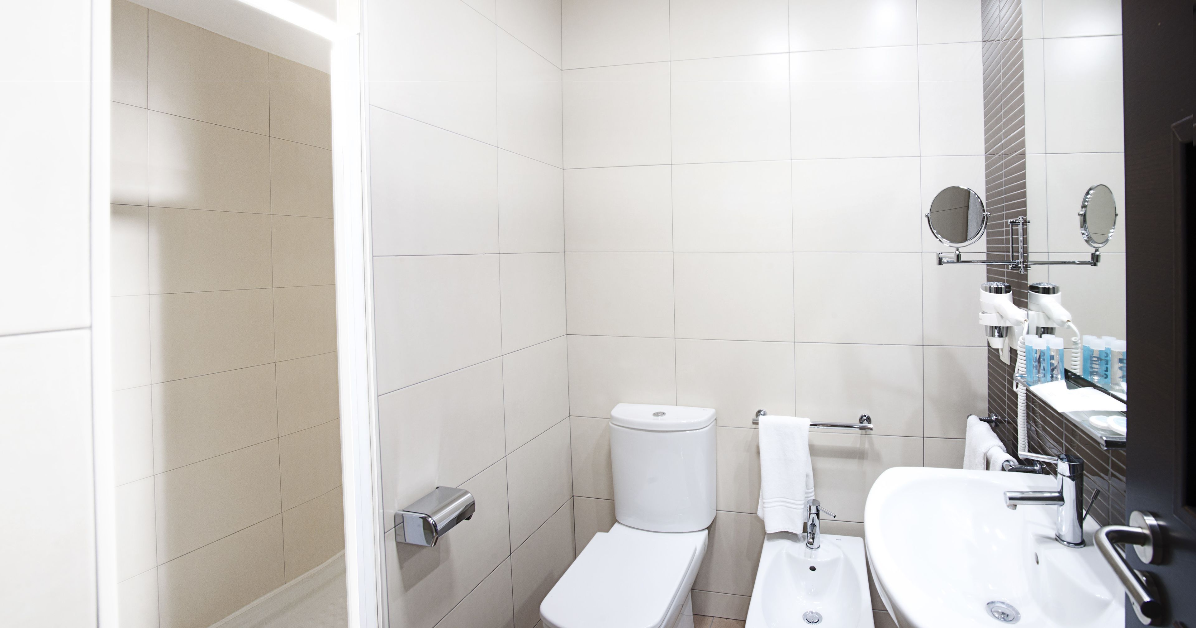 Een moderne badkamer met witte tegels, een toilet, een wastafel en een spiegel.