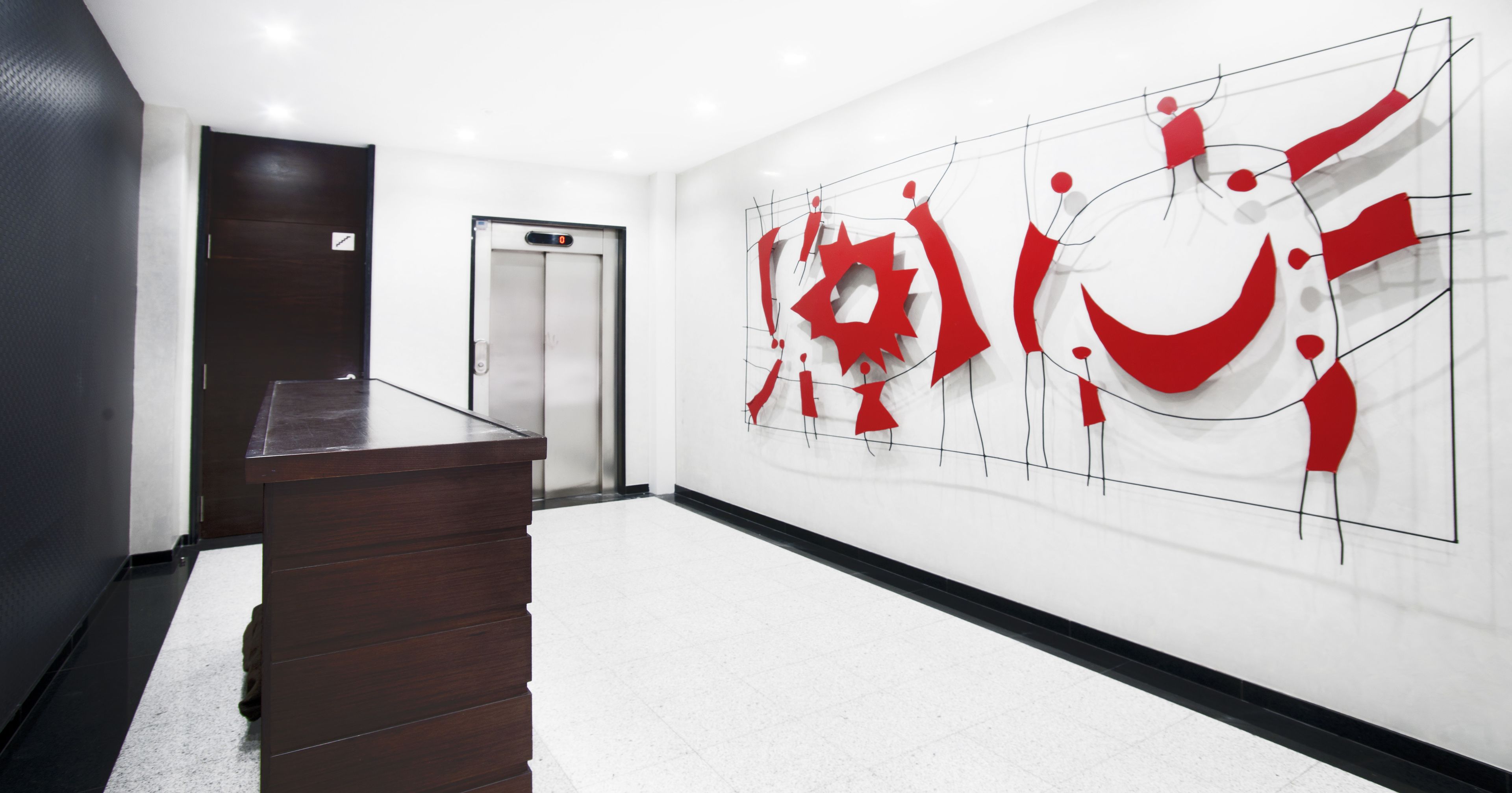 Un vestíbulo moderno con una recepción, un panel digital de ascensor y una gran obra de arte abstracta en la pared.
