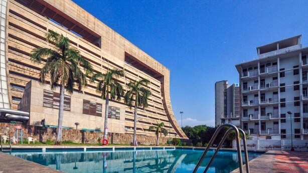 A swimming pool with a modern building in the background. - YMCA Tourist Hostel (New Delhi)