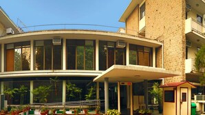 A building with a curved facade, large windows, and a covered entrance area with potted plants. - YMCA Tourist Hostel (New Delhi)