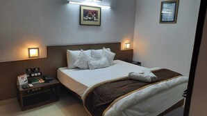 A hotel room with a neatly made bed, a nightstand with a phone and a small table with a book and a sign. - YMCA Tourist Hostel (New Delhi)
