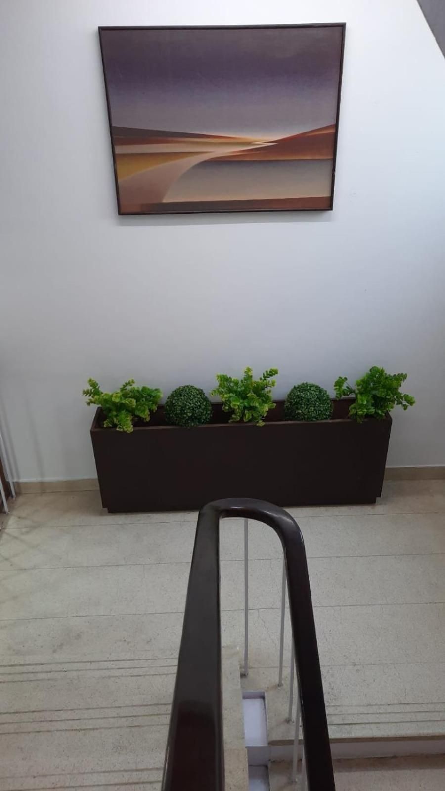 Ein Flur mit einem modernen abstrakten Gemälde an der Wand, einem dunklen Pflanzgefäß mit Grünpflanzen und einem Metallgeländer.