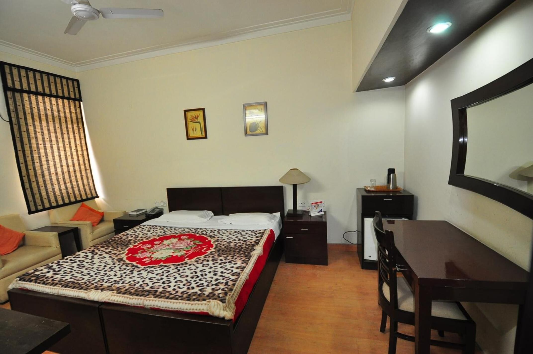 Une chambre à coucher comprenant un lit, un bureau, une chaise, une table de chevet, une lampe et un ventilateur de plafond.