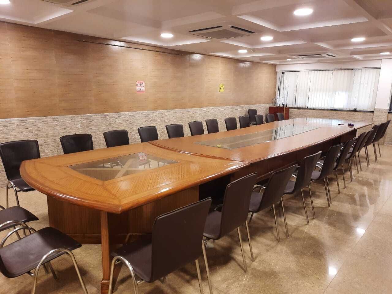 Une salle de conférence avec une longue table en bois entourée de chaises, un sol carrelé et un mur en bois sur lequel est apposée une signalétique indiquant la sortie de secours.