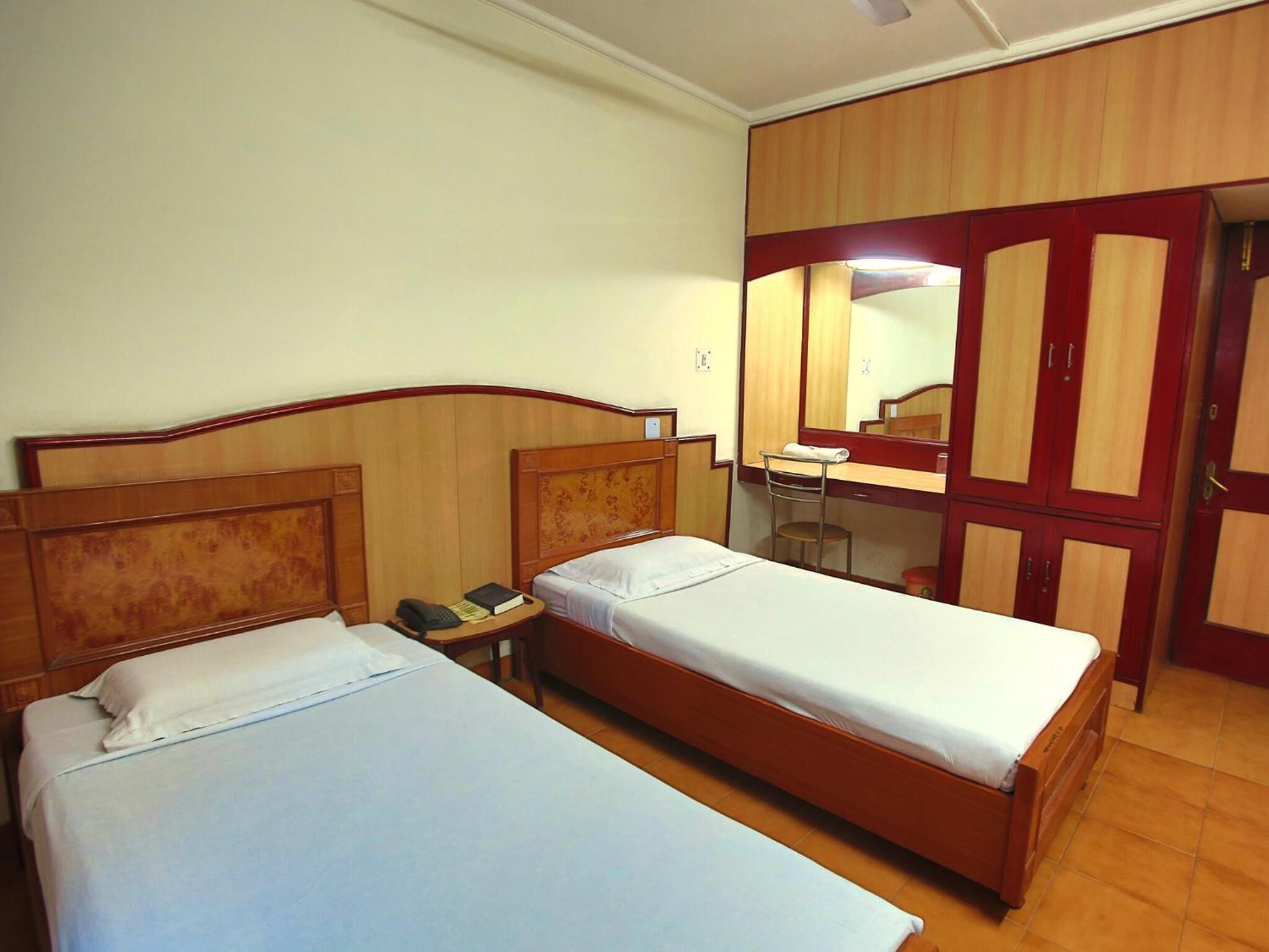 Habitación de hotel con dos camas individuales, un escritorio con silla, un espejo y un armario.