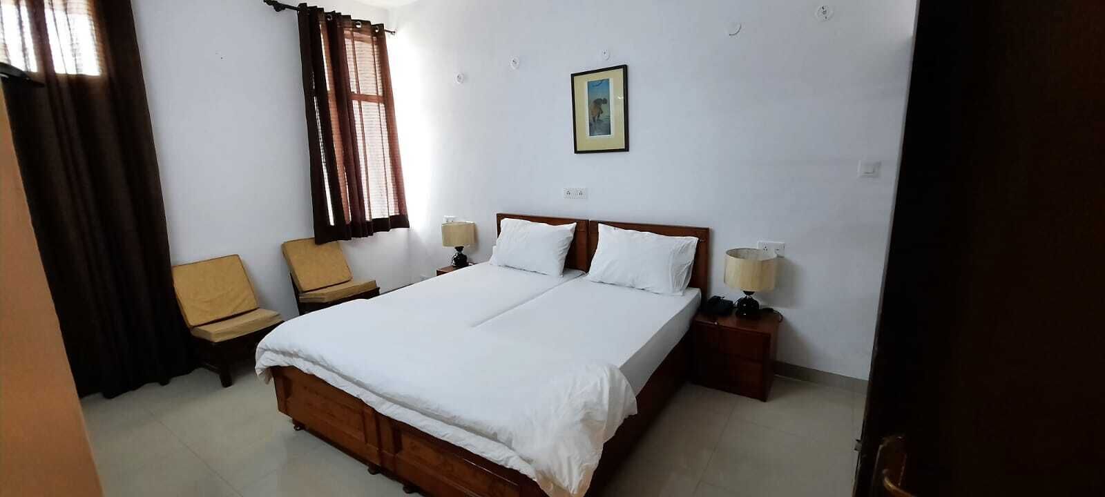 A bedroom with a wooden bed, two bedside tables, a chair, a window with curtains, and a framed picture on the wall.
