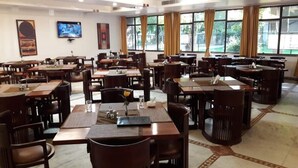 A spacious dining area with multiple tables and chairs, large windows, and artwork on the walls. - YMCA Tourist Hostel (New Delhi)