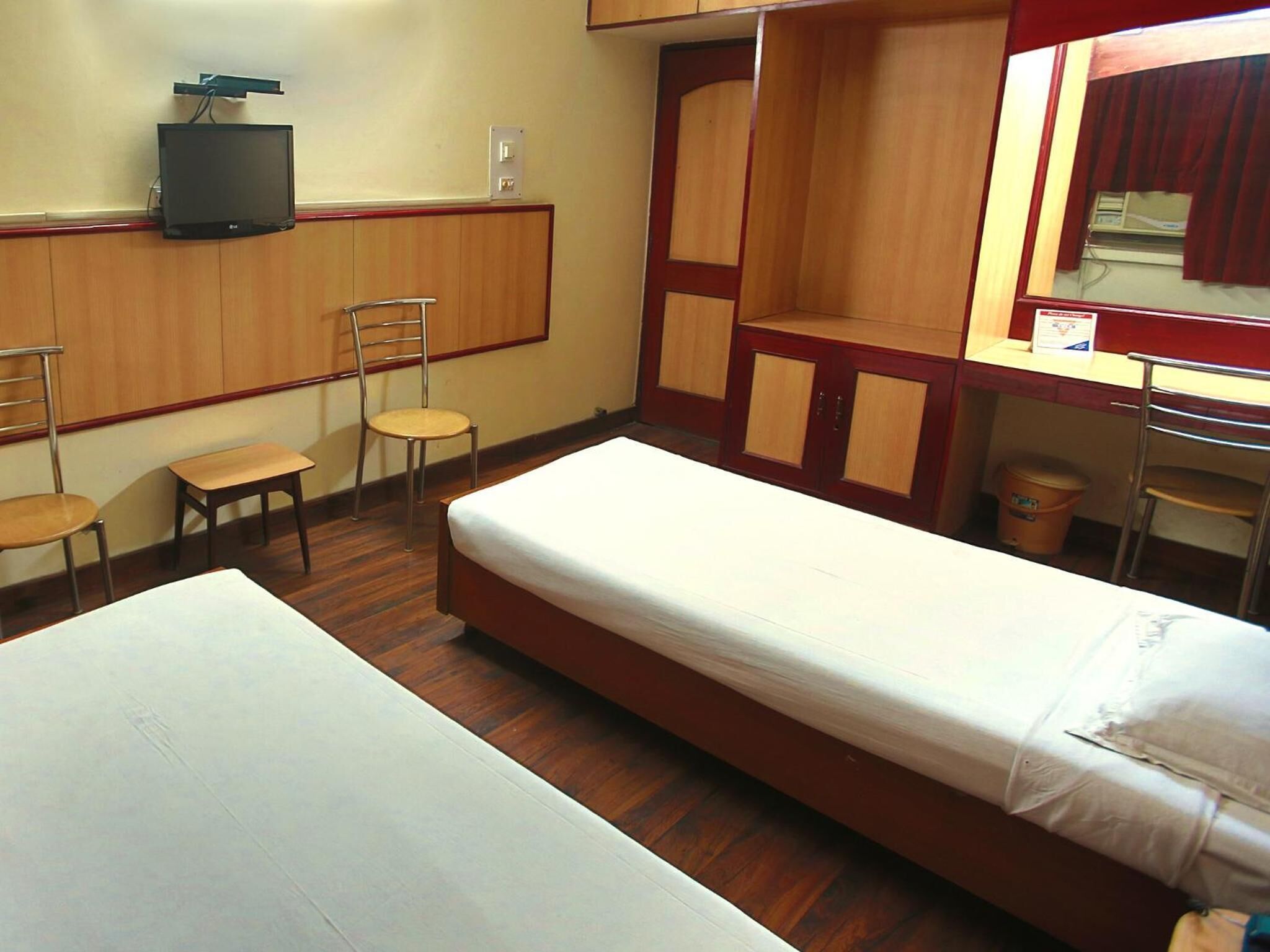 A hotel room with two single beds, a desk with a chair, a television, and a mirror.