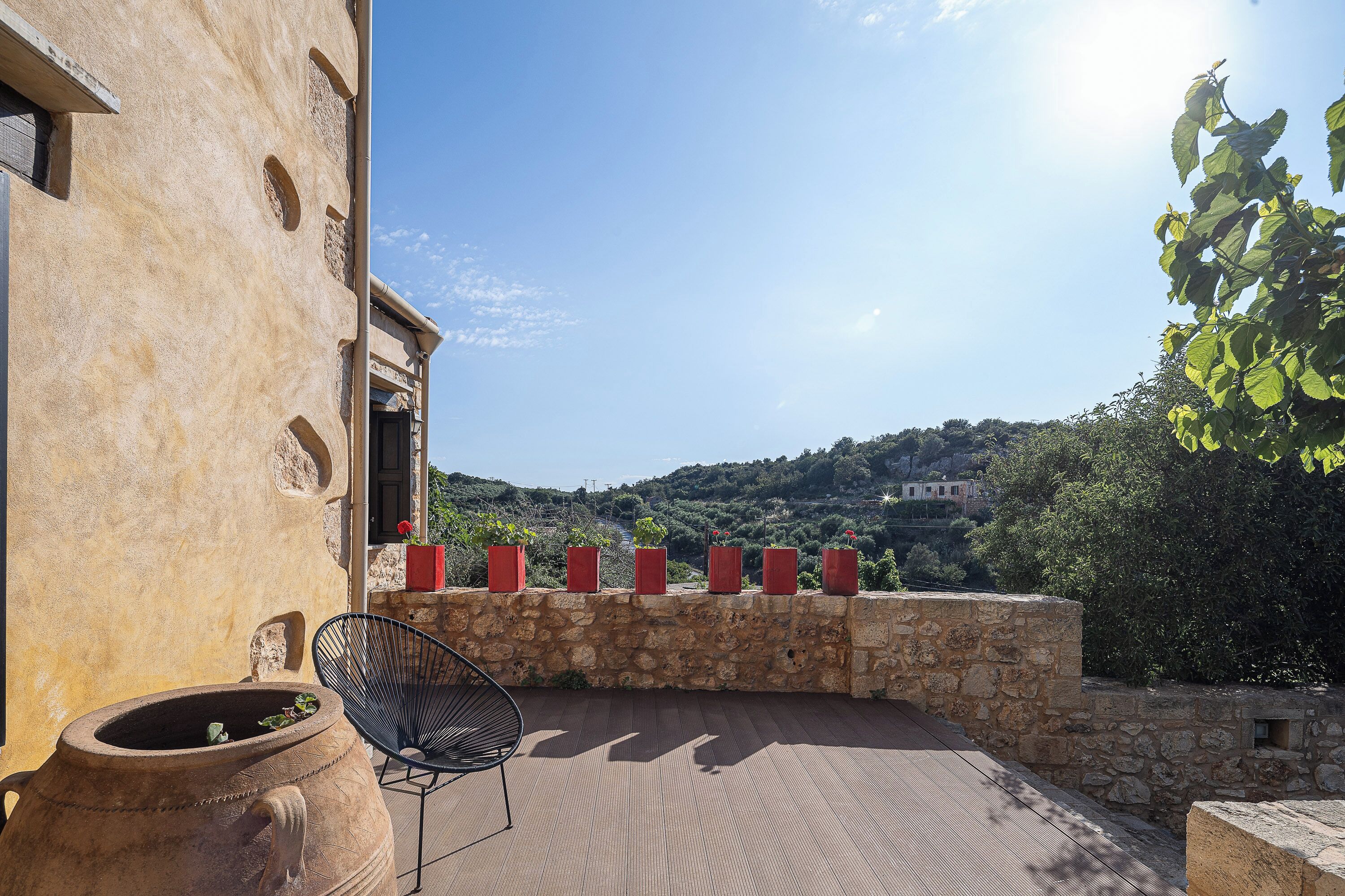 A stone wall with red planters, a black chair, and a view of a hillside.