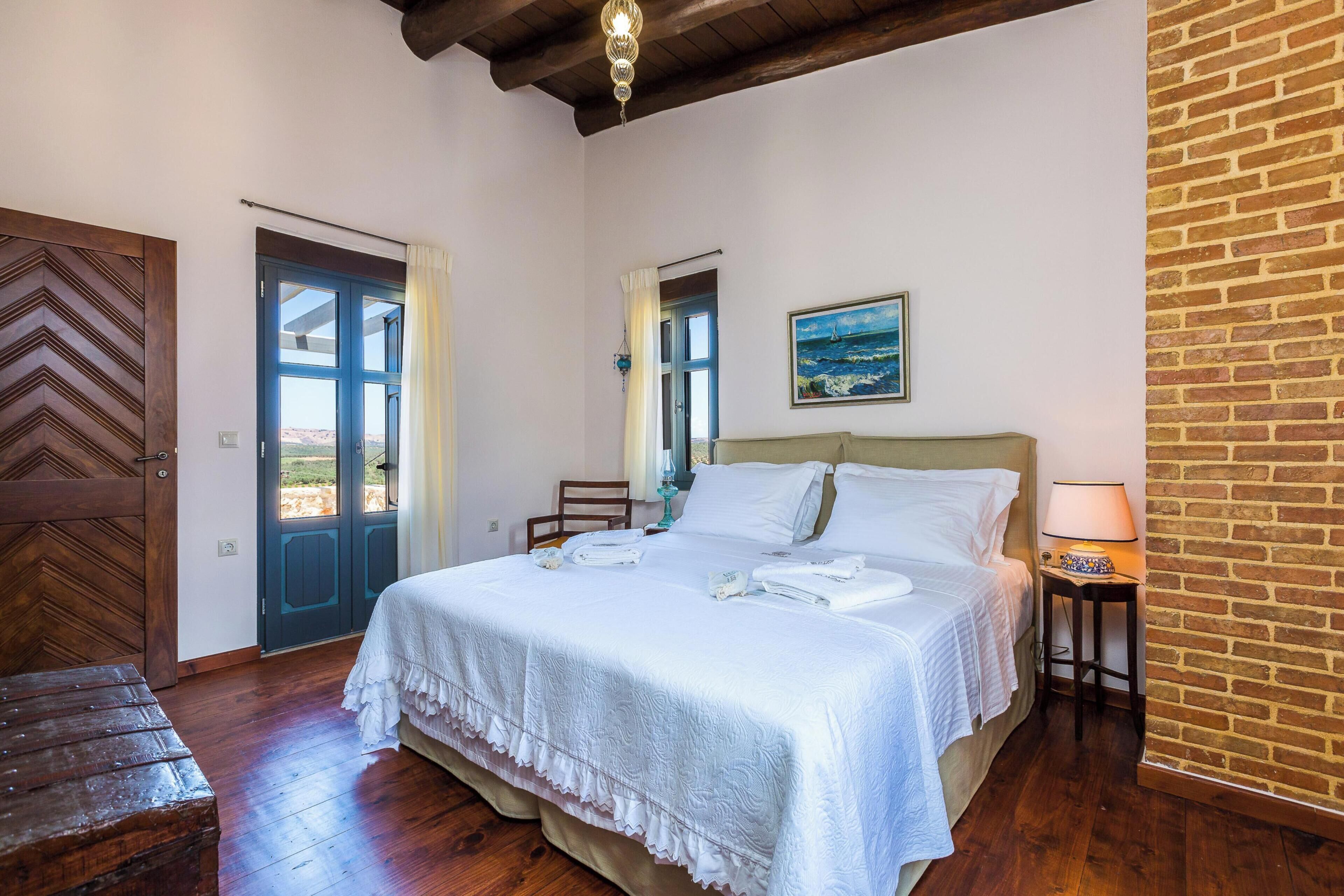A bedroom with a bed, a wooden bench, a door, and a wall with a brick pattern.