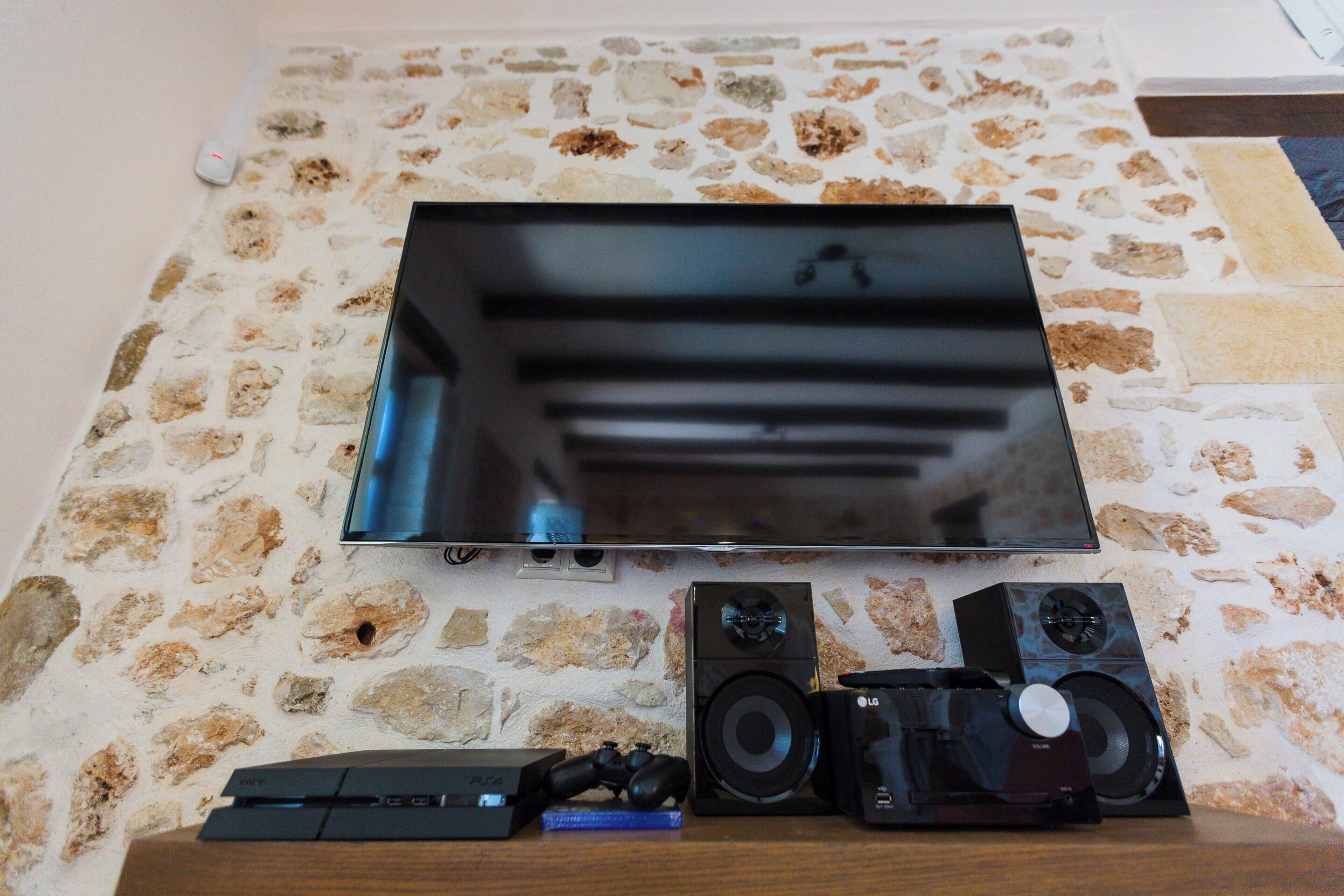 Een flatscreen-televisie bevestigd aan een stenen muur, samen met een soundbar, een camera en een spelconsole.