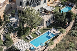 A pool area with lounge chairs, a pergola, and a stone wall.
