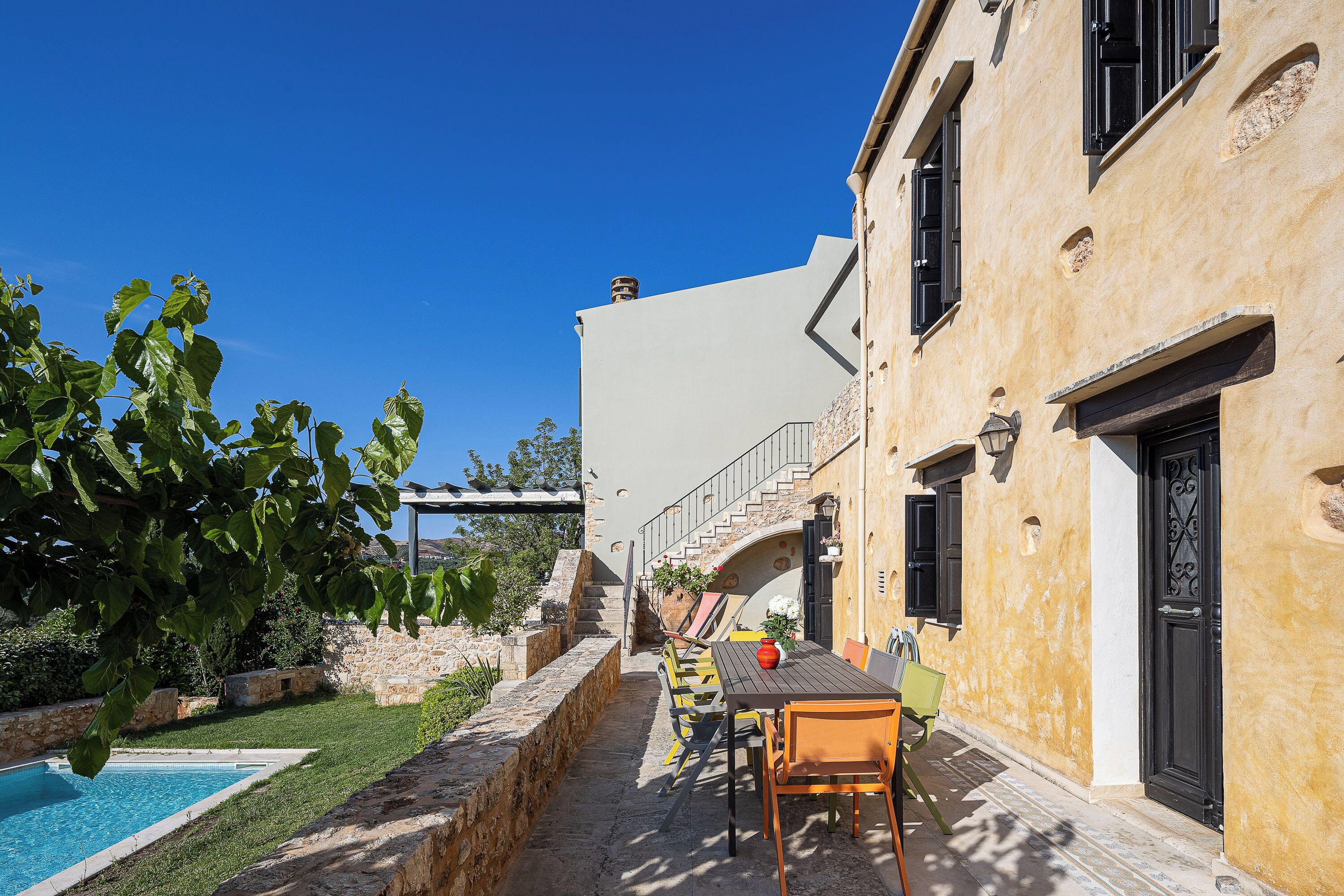 Area piscina con tavolo e sedie, muro in pietra e un edificio con una scalinata.