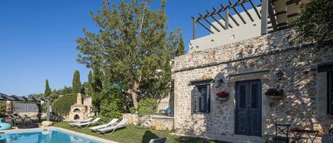 Un bâtiment en pierre doté d’une piscine, de chaises longues et d’une pergola.