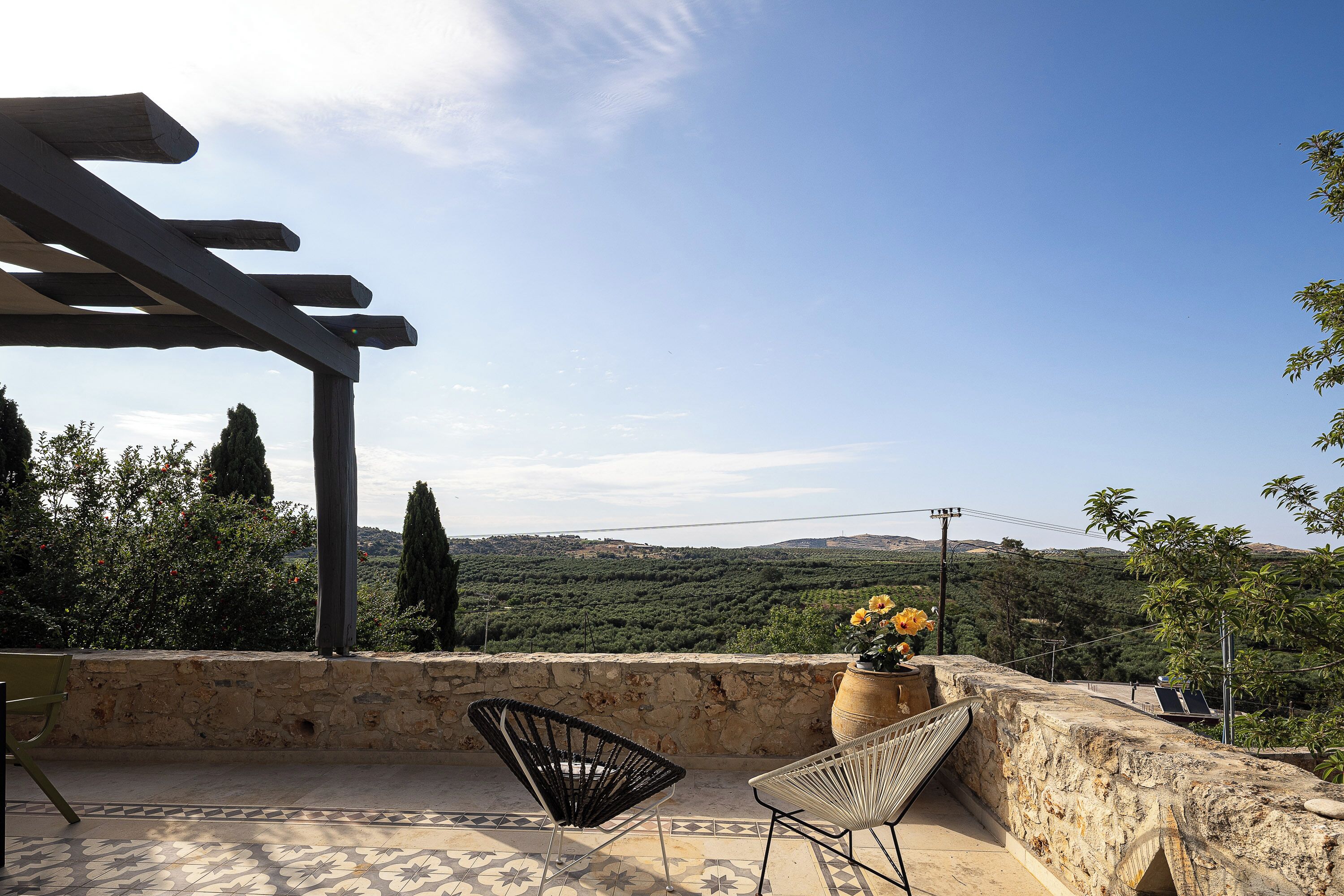 Une terrasse agrémentée d’une pergola, de deux chaises, d’un pot de fleurs et offrant une vue sur un paysage vallonné.