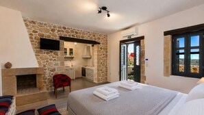 Une chambre avec un mur en pierre, une cheminée, un lit avec des serviettes, une chaise et une vue sur l’extérieur, visible à travers une porte.