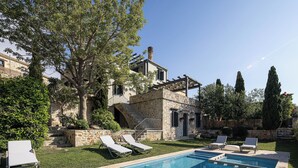 Une piscine avec des chaises longues, un bâtiment en pierre et un arbre.