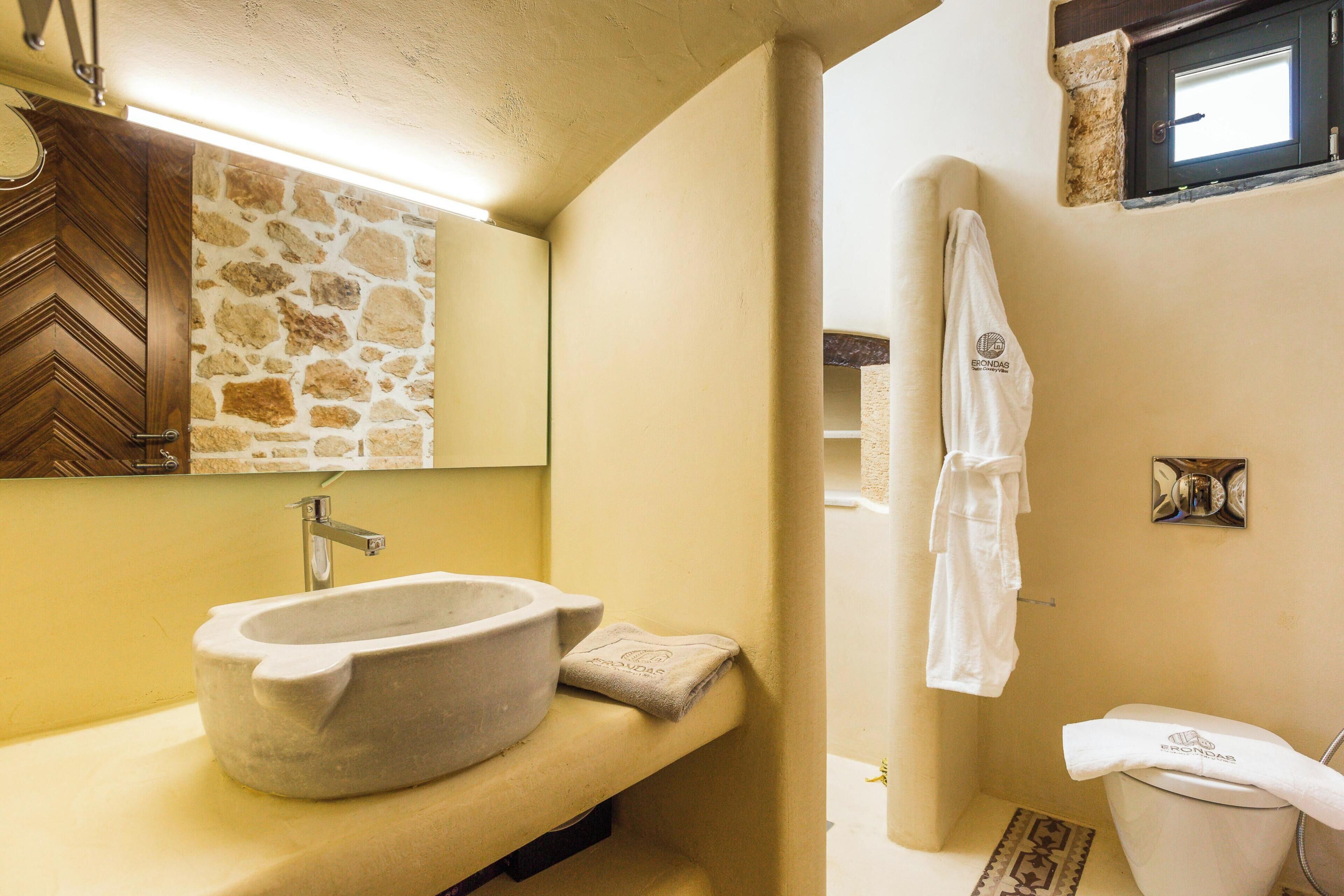A bathroom with a stone sink, a towel, a toilet, and a mirror.