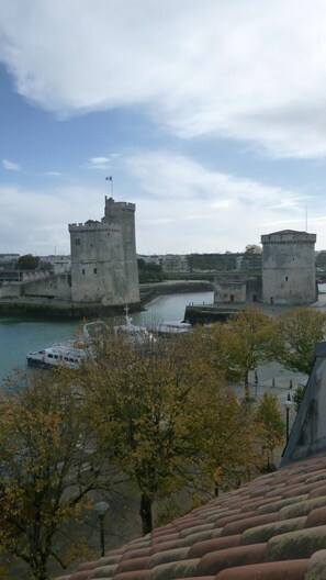 A view of a historic fort with two towers, a river, and a boat docked in the foreground. - Hotel de l'Ocean (La Rochelle)