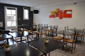 A conference room with multiple tables and chairs, large windows, and abstract paintings on the wall. - Hotel de l'Ocean (La Rochelle)