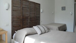 A bedroom with a wooden headboard, two beds, a small table, and a wall-mounted light. - Hotel de l'Ocean (La Rochelle)