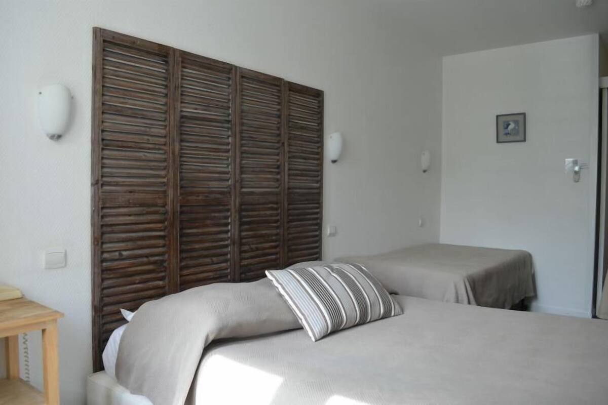 A bedroom with a wooden headboard, two beds, a small table, and a wall-mounted light.
