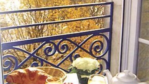 A balcony with a table set for breakfast, including bread, tomatoes, juice, and a teapot. A castle is visible in the background. - Hotel de l'Ocean (La Rochelle)