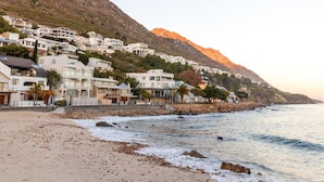 A coastal town with white buildings, a sandy beach, and a rocky hillside. - The View (Cape Town)