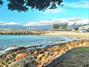 A rocky shoreline with a clear view of the sea, a sandy beach, and a marina with boats. - The View (Cape Town)