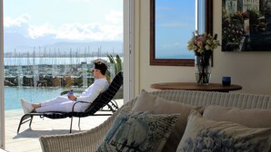A man relaxing on a chair by a large window overlooking a marina with boats. - The View (Cape Town)