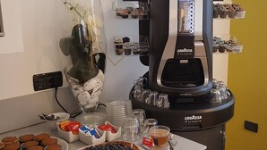 A coffee machine with multiple cups and a variety of coffee pods. There are also several cups and a bowl of snacks on the table. - Hotel San Marco BB (Darfo Boario Terme)