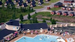 A large swimming pool with a water slide, surrounded by a building with a flat roof and a covered area with seating. - Hotell Kraja (Arjeplog)