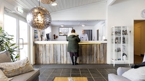 A reception area with a wooden reception desk, a coffee table with a plant, and a seating area with sofas. - Hotell Kraja (Arjeplog)