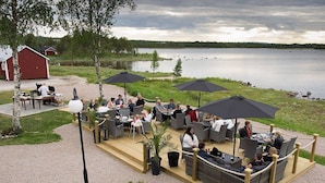 An outdoor seating area with tables and chairs, surrounded by umbrellas, overlooking a lake. - Hotell Kraja (Arjeplog)