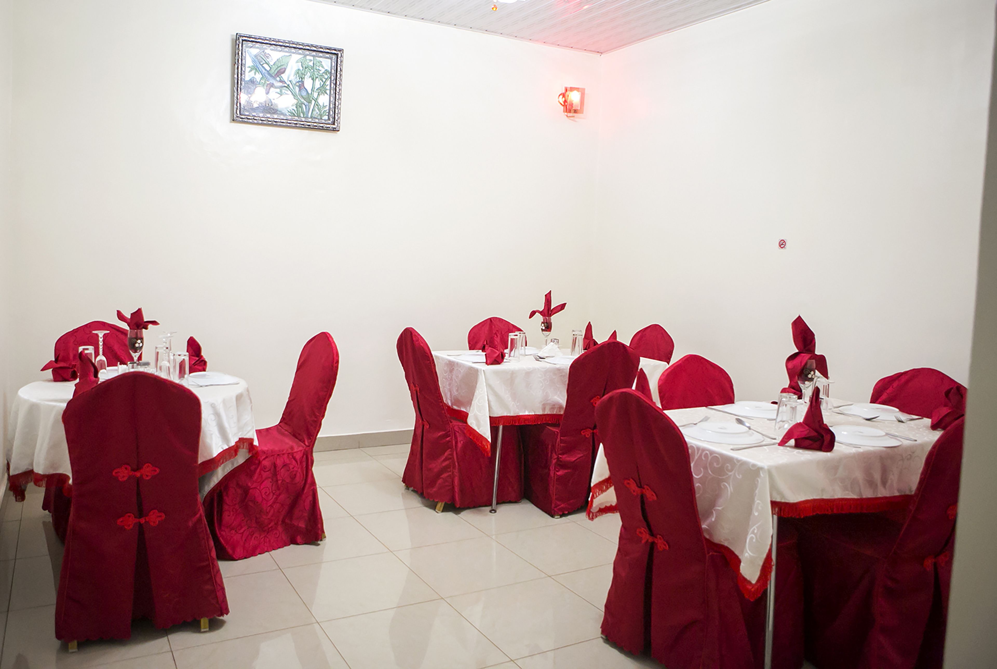 A dining area with tables set for four, each with white tablecloths and red chair covers.