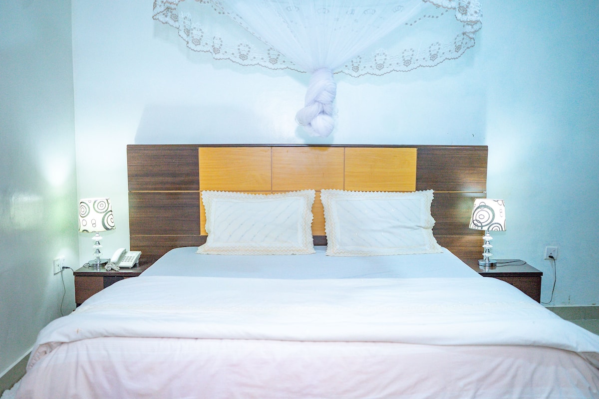 A neatly made bed with a wooden headboard, two bedside lamps, and a wall-mounted decorative item.