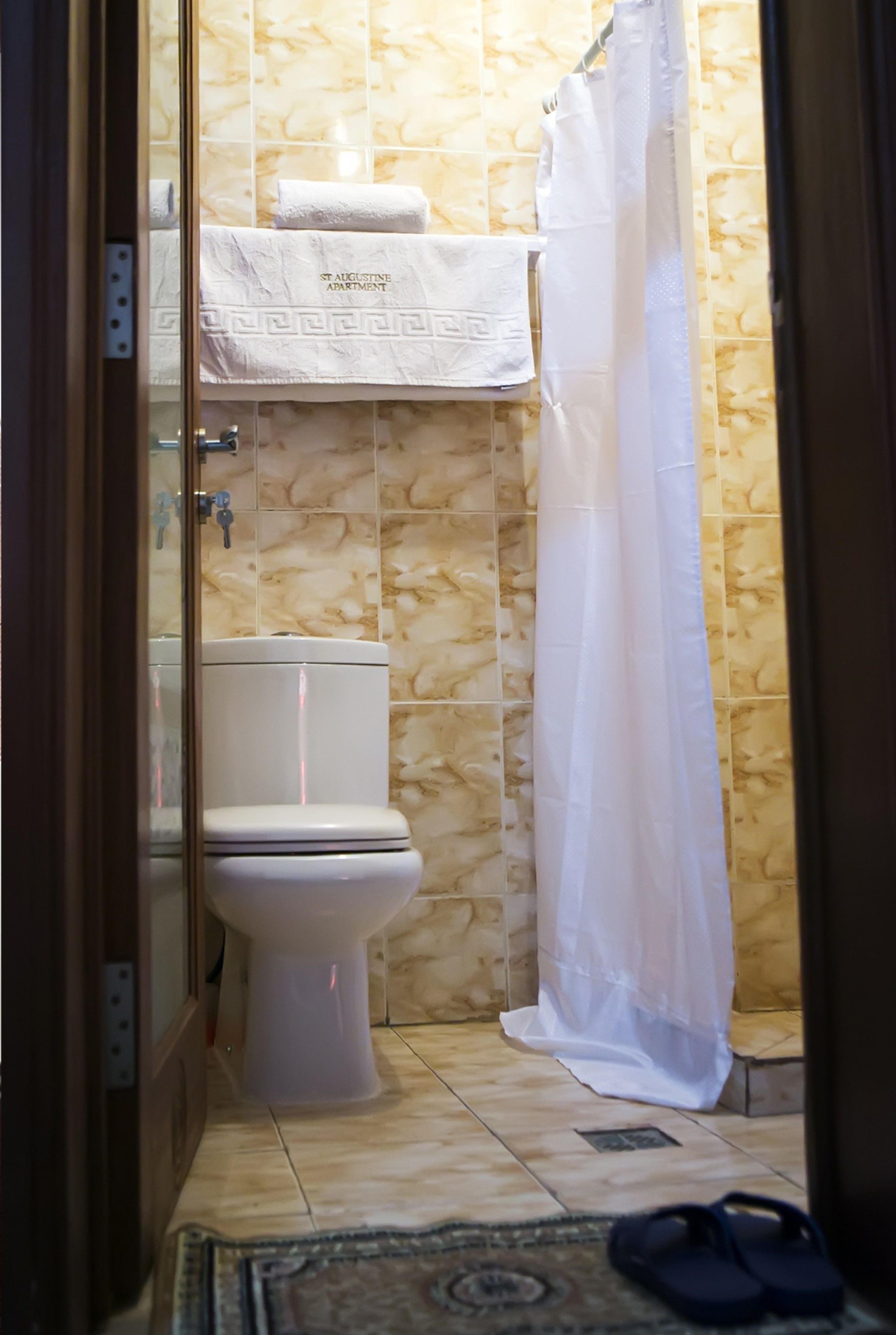 A bathroom with a toilet, a shower curtain, and a towel with "ST. AUGUSTINE APARTMENT" text.