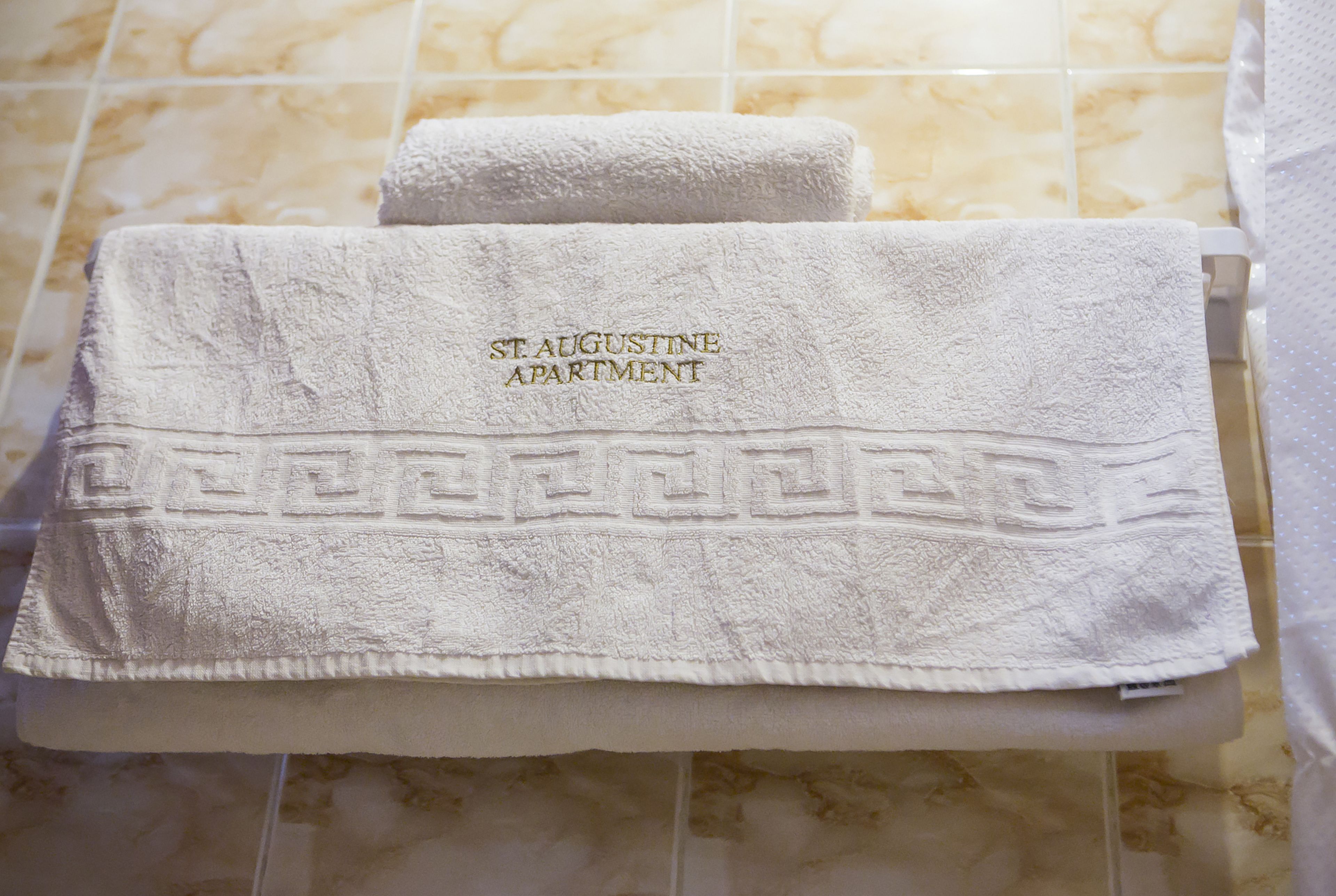 Ein gefaltetes weißes Handtuch mit dem Aufdruck "ST. AUGUSTINE APARTMENT" auf einem gefliesten Boden.
