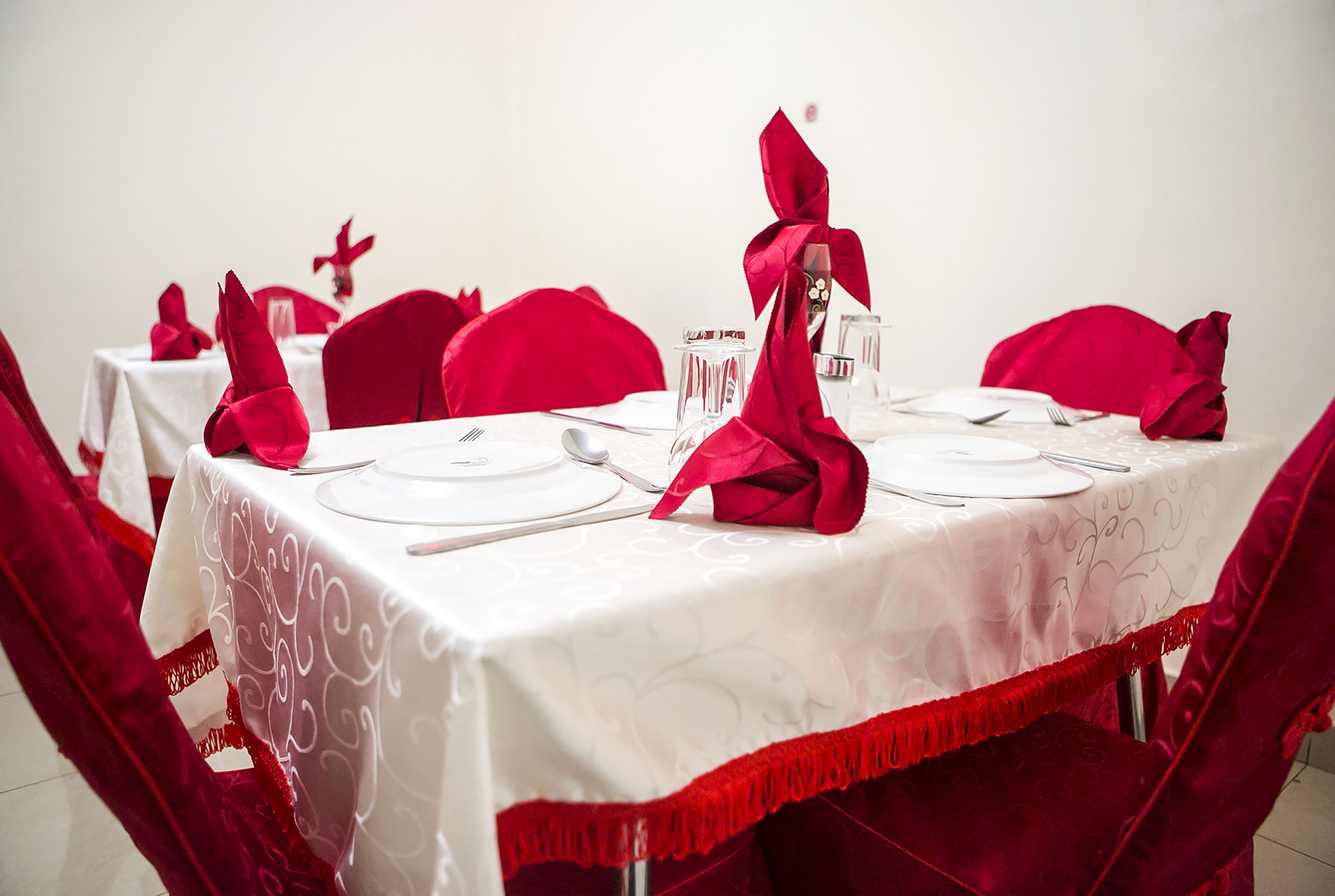A table set with white tablecloths, red napkins, and clear glassware.