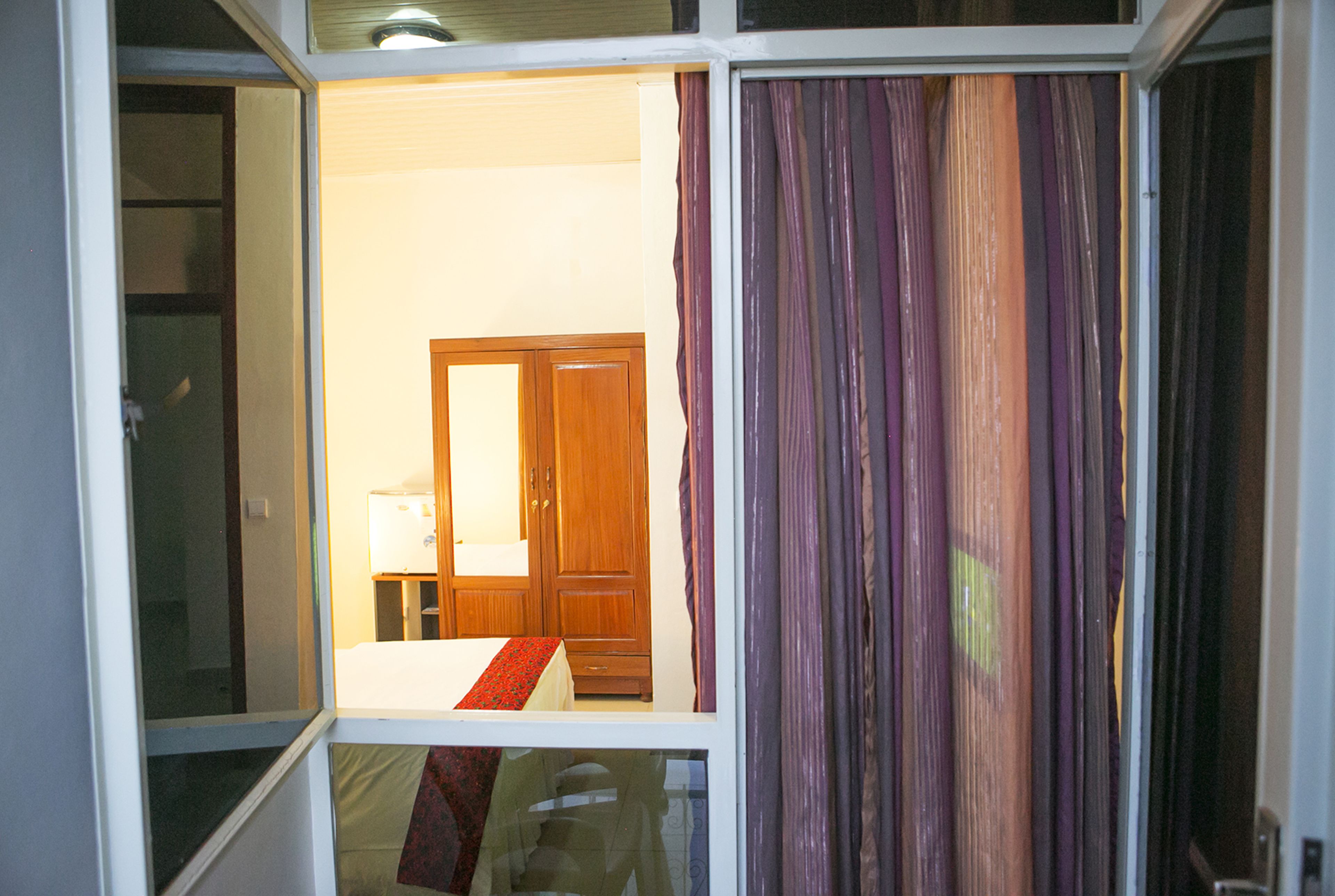 A room with a bed, a wooden wardrobe, and a window with purple curtains.