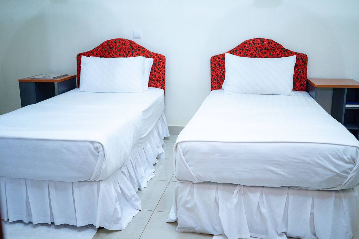Two single beds with red floral headboards and white bedding, each with a wooden nightstand beside.