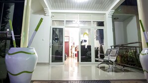 Una entrada de hotel con puerta de cristal, un mostrador de recepción y un área de espera con sillas.
