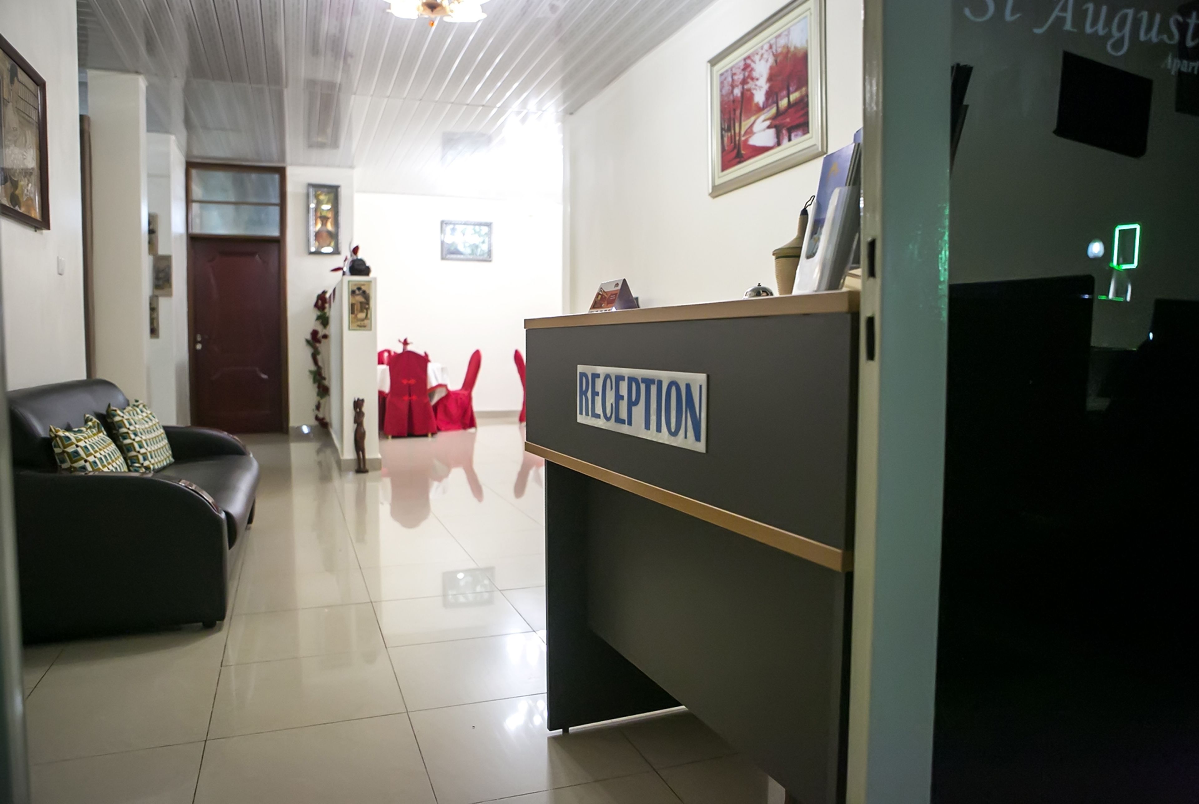 A reception area with a reception desk labeled "RECEPTION," a black leather sofa with patterned cushions, a red chair, and a door in the background.