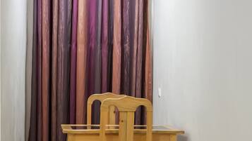 Un pasillo estrecho con una silla y una mesa de madera, una cortina y un piso de baldosas.